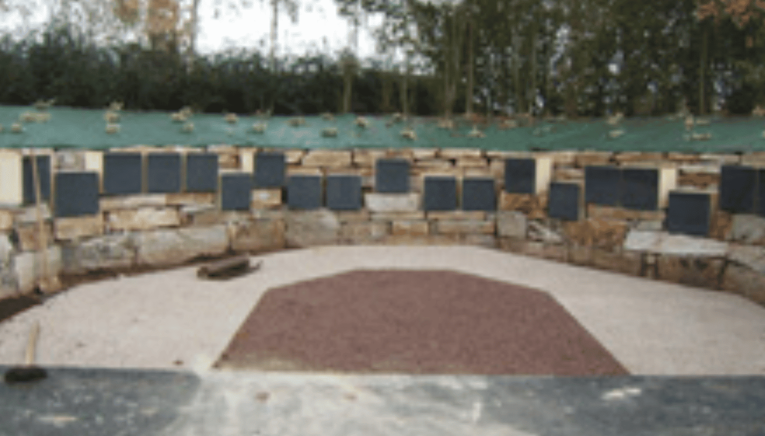 cavurnes posées sur un mur de pierres et organisées en demi cercle. Exemple d'un aménagement cinéraire. Fabricant Stradal Funéraire